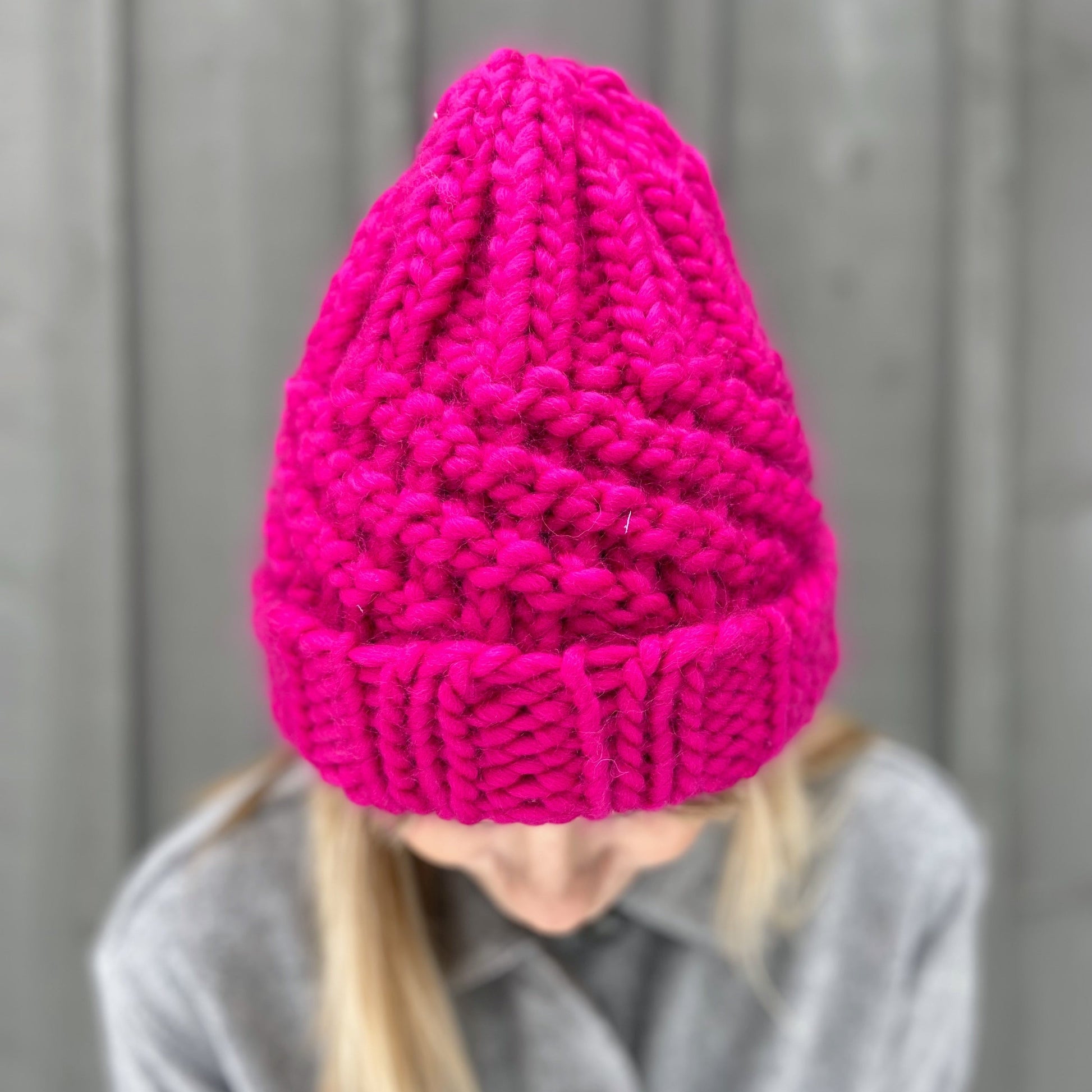 Woman wearing a bright fuchsia coloured chunky knit beanie.