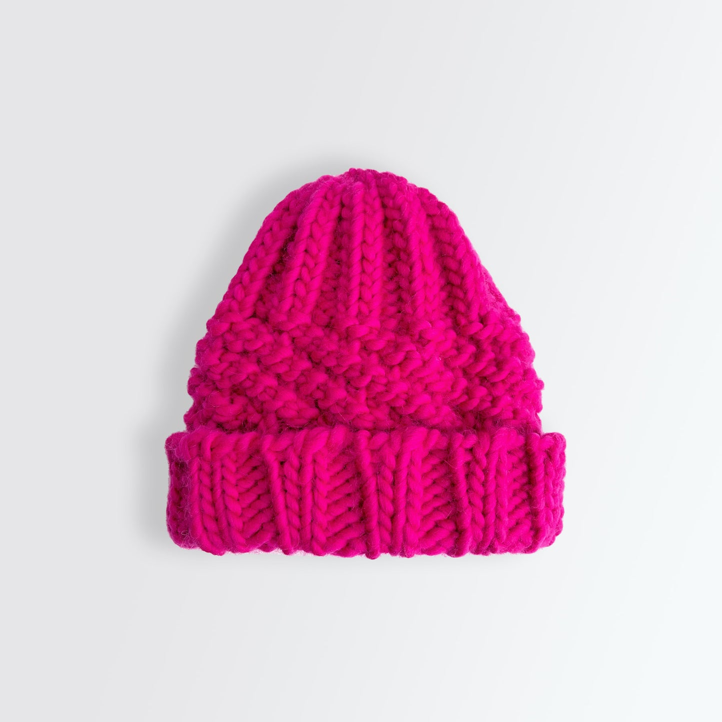 A bright fuchsia coloured chunky knit beanie on white background..